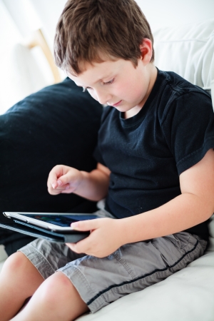 Boy playing on a tablet while sitting on a couchの写真素材
