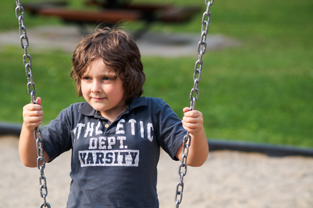 Boy sitting on a swing in a playgroundの写真素材