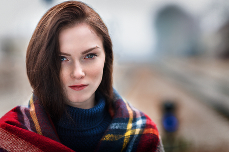 The girl with a woolen scarf looks in a camera. Behind the girl the railroad. Portrait of the young woman.の写真素材