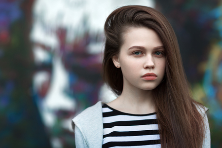 The girl in a t-shirt with long nutbrown hair look in camera. The graffiti in the background.の写真素材