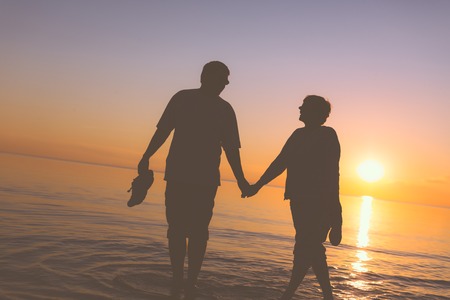 Happy senior couple silhouettes on the beachの写真素材