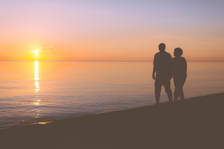 Senior couple walking along the beach at sunsetの写真素材