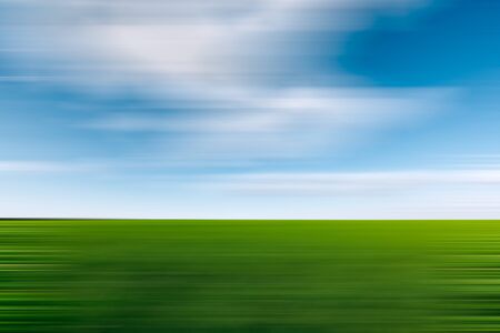Green field and blue sky with clouds. Green with blue motion blur abstract background with horizontal stripesの写真素材