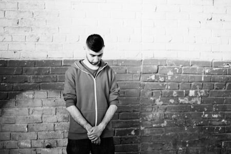 Young man near the brick wall folded his hands and looking down.の写真素材