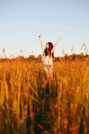 Girl in a field stretched hands in the air.の写真素材