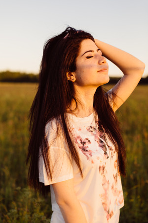 Girl straightens her hair with her eyes closed in field.の写真素材