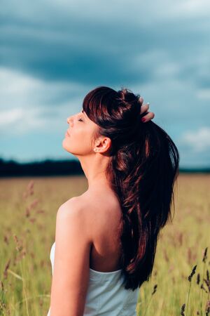 Portrait of young woman. Young woman adjusts her hair against a green field.の写真素材