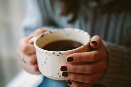 Close up of a  young woman hands holding a cup of hot coffee.