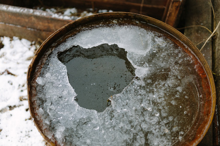 Broken ice in an old rusty barrel closeup photo.の写真素材