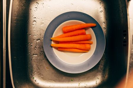 Peeled washed up carrots in a plate in a silver sink. Close up photo top view.の写真素材