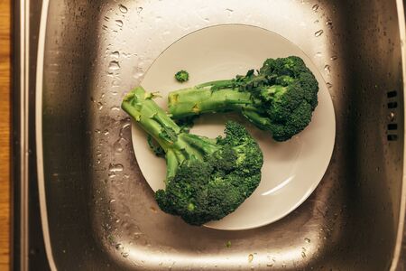 Peeled washed up broccolis in a plate in a silver sink. Close up photo top view.の写真素材