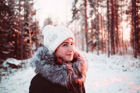 Girl in a white hat and a jacket on a background of a winter forest. Close up photo.の写真素材