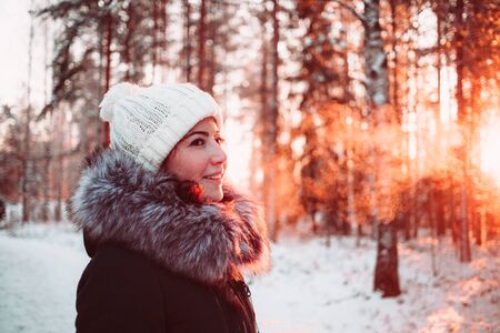 Young woman in a white hat and a jacket on a background of a winter forest. Close up photo.の写真素材