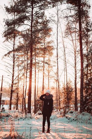 Pretty girl in a white hat and a jacket on a background of a winter forest. Photo girl in full growth.の写真素材