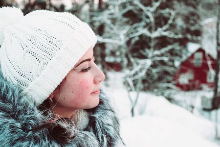 Young woman in a white cap and a jacket on a background of a winter forest. Close up photo.の写真素材