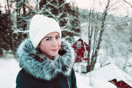 Beautiful young woman in a white cap and a jacket on a background of a winter forest. Close up photo.の写真素材