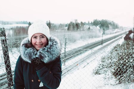 Beautiful girl in a white hat and a jacket on a background of a winter rails. Close up photo.の写真素材