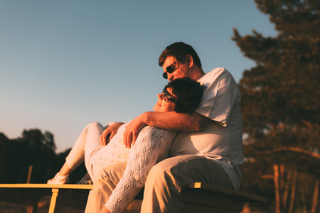 Adult married couple on a bench. Husband embraces his wife.の写真素材