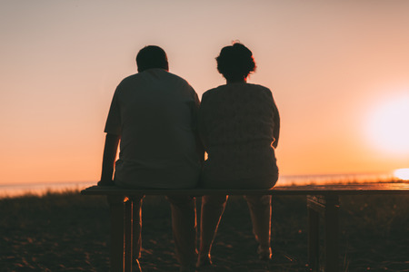 Back view a married couple a silhouette sitting on a bench. Evening photo.の写真素材