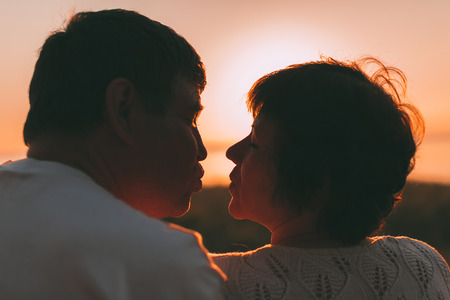 Adult married couple last to each other to kiss. Photo against a sunset.の写真素材