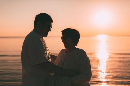 Back view of a couple silhouette watching sun at sunset on the beach with light.の写真素材