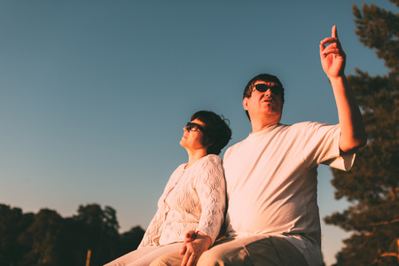 Adult couple sitting on a bench and looking at the sky. Side view photo.の写真素材