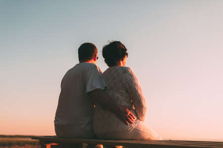 Back view of a couple silhouette watching sun at sunset on the beach with light.の写真素材