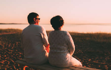 Back view a married couple a silhouette sitting on a bench. Evening photo.の写真素材