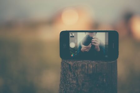 Photographer photographing themselves using a smartphone as a mirror. Modern photo.の写真素材