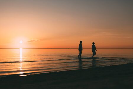Silhouette of adult couple standing in the sea against a sunset. Evening photo.の写真素材