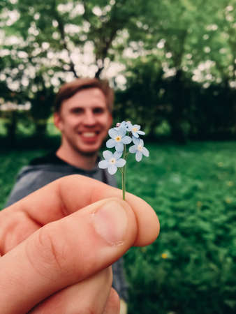 Fingers holding a small flower on the background of young man.の写真素材