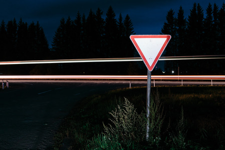 Road sign give way. Road sign at night on the background traffic at long exposure.