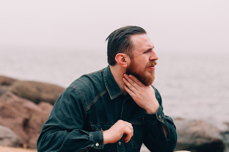 Serious Bearded man clutched his neck. bearded hipster on the beachの写真素材