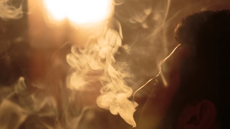 young bearded man breathes out clouds of white smoke