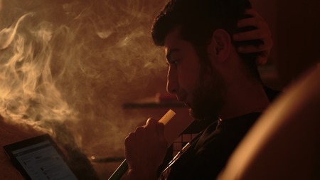 young man smokes a hookah and uses tablet