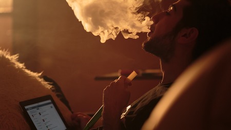 young man smokes a hookah and uses tablet