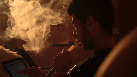 young man smokes a hookah and uses tablet