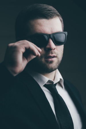 Portrait of a young trendy man in sunglasses lowered a little in the dark room close upの写真素材