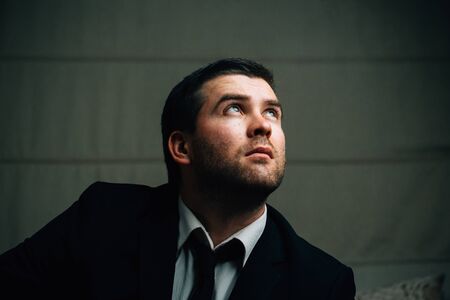 Young businessman looks up the light in a dark roomの写真素材