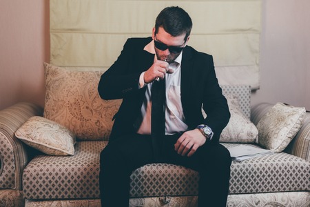 Young businessman smoking a e-cigarette while sitting on the couchの写真素材