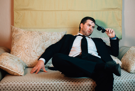 Young stylish businessman with sunglasses sitting on the couchの写真素材