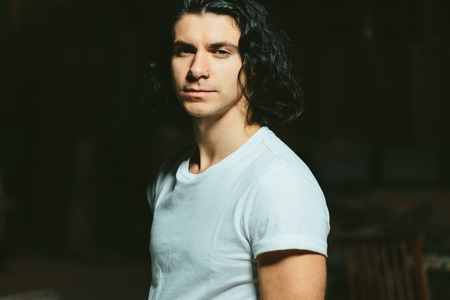 Portrait of a beautiful brutal guy with long hair on a dark background
