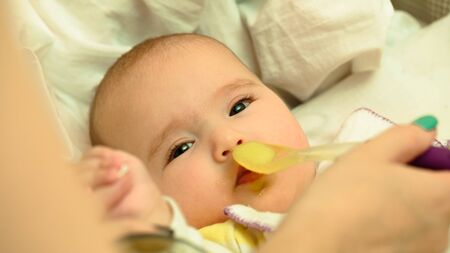 Mother feeds her little child baby puree with spoon close-up