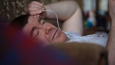 middle-aged man lying on the couch and listen to music from your gadget closeupの写真素材