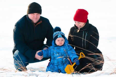 Young family playing with their child in the snow in the parkの写真素材