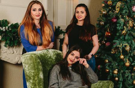 Three beautiful young girls near the Christmas tree. Studio horizontal close-up portrait
