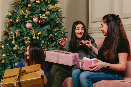 Three beautiful young girls unpack gifts near a Christmas tree. Studio horizontal portraitの写真素材