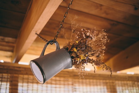 Metal vase with dry plants and flowers hung on the ceiling with a chain.の写真素材