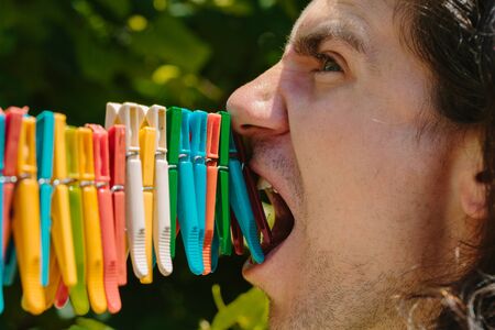 Man tries to bite off clothes pegs. Side view.の写真素材