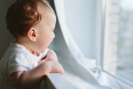 Little baby holds onto the bed and looks somewhere. Photo in the daytime.の写真素材